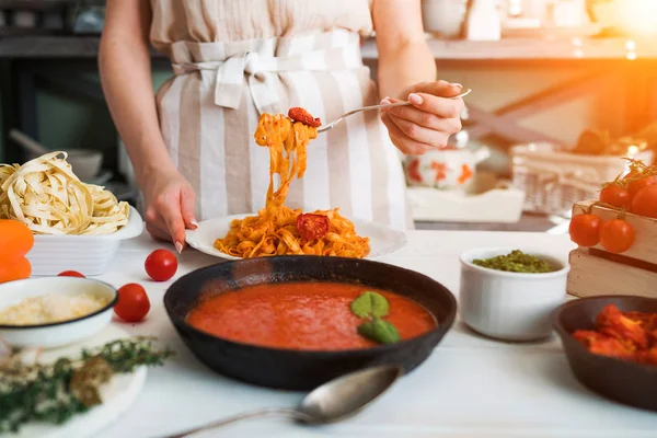 Italian style pasta dinner. Pasta with tomato and basil in plate on the wooden rustic table and ingredients for cooking. Chef hands preparing delicious pasta with tomato sous. Homemade food.