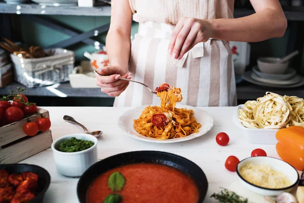 Italian style pasta dinner. Pasta with tomato and basil in plate on the wooden rustic table and ingredients for cooking. Chef hands preparing delicious pasta with tomato sous. Homemade food.