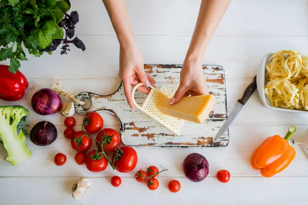 Female woman hands cut cheese on white rural wooden kitchen table with vegetables cooking ingredients and tools, top view. Food background. Food concept with various fresh Ingredients.