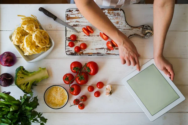 Cooking, culinary, food, technology and people concept. Young woman using a tablet computer to cook in her kitchen. A woman searching the cooking menu and preparing food ingredient before cooking.