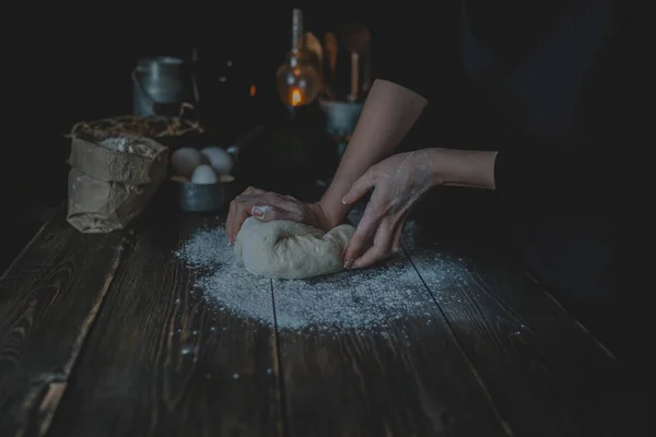 Female hands holding dough in ball shape. Basic homemade dough with ingredients on the side on wooden table with natural light. Home healthy food. Selective focus. Focus on the dough.