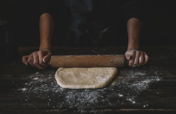 Dough with rolling pin on kitchen table. Rolling out a circle of pizza dough with a wooden rolling pin. Food, cooking and baking concept. Flour, egg on vintage wooden table. Rustic background with copy space.