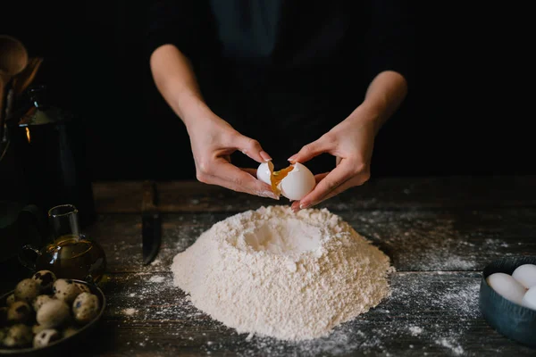 焼成過程で素朴な木製のテーブルで小麦粉に卵を注いだ 暗い木製のテーブルに食材を焼きます パンを作る レトロなイメージ 粒追加 選択と集中 — ストック写真
