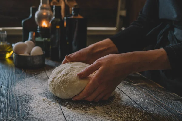 Female hands holding dough in ball shape. Basic homemade dough with ingredients on the side on wooden table with natural light. Home healthy food. Selective focus. Focus on the dough.