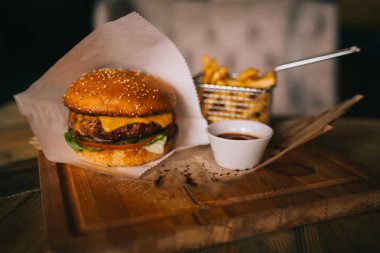 Fast food yemek. Kraft kağıt, patates cipsi et burgeri. Patates kızartması, hamburger, mayonez ve soslar ahşap üzerinde. Menü veya tarifi arka plan. Patates kızartması ufaklık sepet ve ketçap kase.