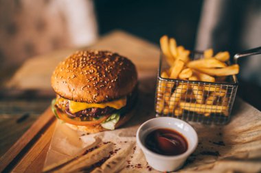Lezzetli sığır eti burger taze patates ile. Fast food kavramı. Izgara sığır eti burger marul ve mayonez rustik ahşap masa üzerinde kahverengi kağıt parçaları yılları arasında görev yapmıştır. Bir Amerikan burger patates kızartması ile
