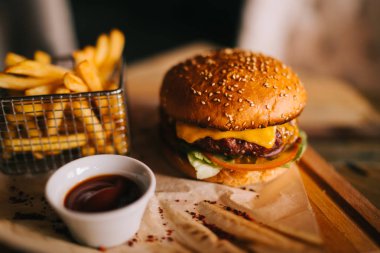 Lezzetli sığır eti burger taze patates ile. Fast food kavramı. Izgara sığır eti burger marul ve mayonez rustik ahşap masa üzerinde kahverengi kağıt parçaları yılları arasında görev yapmıştır. Bir Amerikan burger patates kızartması ile