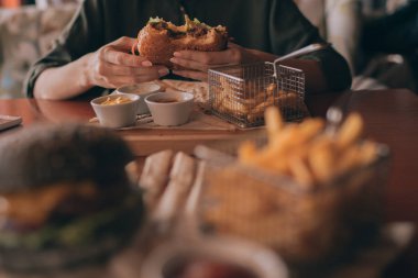 El lokanta hamburger, Amerikan sağlıksız kalori yemek tutan genç kız. Izgara hamburger önden görünüm aç insan. İnsanlar ve beslenme kavramı. Fast food. Tonlu görüntü.