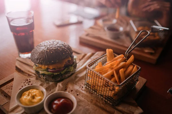 Tasty burger and sauce on wooden tray. Woman eating burger and chips in cafe. People and eating concept. Hamburger, french fries, ketchup, mustard on a wooden board. Toned image.