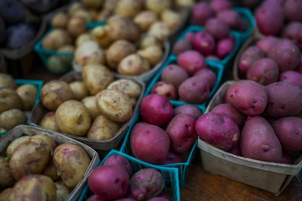 Organic potatoes. Farm fresh vegetable. Beautifully displayed in attractive baskets. Eco potatoes on sale at outdoor farmers market. Raw potato food. Different varieties of potatoes in a shelf.