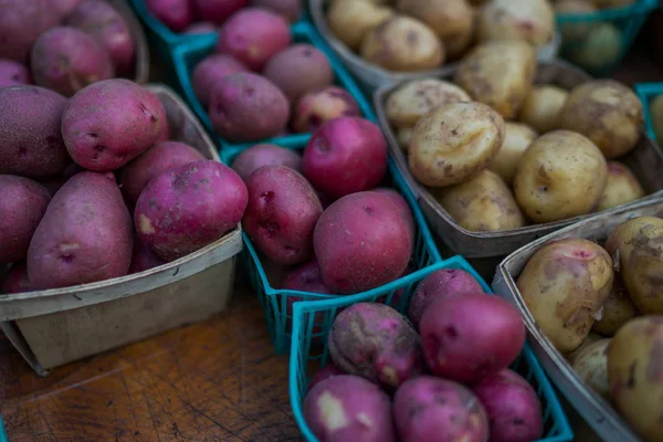 Organic potatoes. Farm fresh vegetable. Beautifully displayed in attractive baskets. Eco potatoes on sale at outdoor farmers market. Raw potato food. Different varieties of potatoes in a shelf.