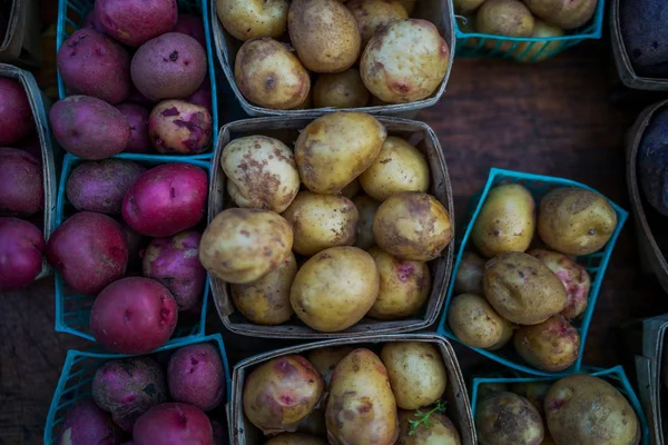 Organic potatoes. Farm fresh vegetable. Beautifully displayed in attractive baskets. Eco potatoes on sale at outdoor farmers market. Raw potato food. Different varieties of potatoes in a shelf.