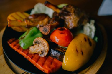 Yemek ve eğlence kavramı. Yemek masada. Sebze ve otlar bir kavurma demir Pan ile lezzetli ızgara kuzu bacak. Çeşitli lezzetli sebze ızgara et ile. Tonlu görüntü. Seçici odak.