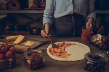 Pizza yapma süreci. Hamur el Tepesi hazırlayın. Kadın el pastörize domates salçası bir pizza tabanı üzerine yayılıyor. Gıda kavramı. Geleneksel İtalyan pizza hazırlanıyor. Tonlu görüntü.