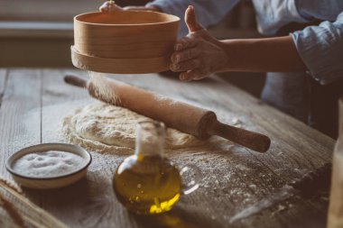 Ev yapımı çiğ hamur rustik ahşap bir masa üzerinde. Pizza yapma. Bir oklava ile hamur. Un, tereyağı, buğday spikelets. Yemek ve gıda kavramı. Tonlu görüntü.