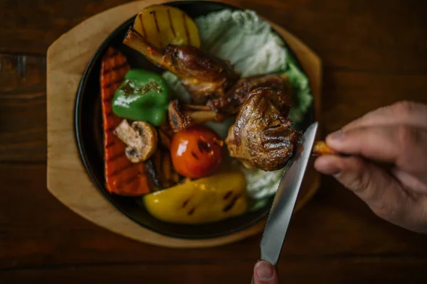 Eating and leisure concept. Dinner on the table. Tasty grilled lamb leg with vegetables and herbs on a roasting iron pan. Assorted delicious vegetables with grilled meat. Toned image. Selective focus.