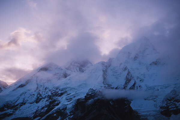 Himalayas landscape. Mountain range with trail in mist and clouds, dark sky with dim sunlight in the background. Stormy weather in mountains. Trekking in Himalaya mountains, Nepal. Nature landscape.