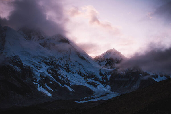 Himalayas landscape. Mountain range with trail in mist and clouds, dark sky with dim sunlight in the background. Stormy weather in mountains. Trekking in Himalaya mountains, Nepal. Nature landscape.