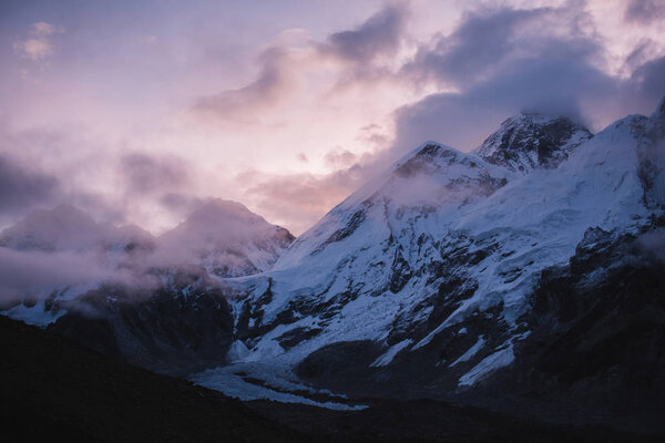 Himalayas landscape. Mountain range with trail in mist and clouds, dark sky with dim sunlight in the background. Stormy weather in mountains. Trekking in Himalaya mountains, Nepal. Nature landscape.