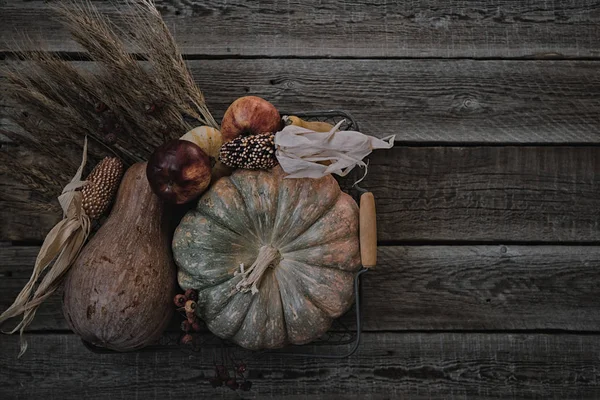 Thanksgiving background. Pumpkins, apples, leaves, ears of wheat and spices on brown wooden background. Seasonal fall background for Thanksgiving or Halloween. Design mock up. Horizontal, toned image.