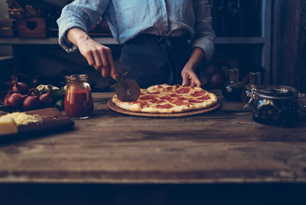 Cook\'s hands making homemade pizza on the table. Pizza with ingredients. Tomatoes, garlic, parsley, pepper, and parmesan cheese on dark wooden background. Food, family and people concept.