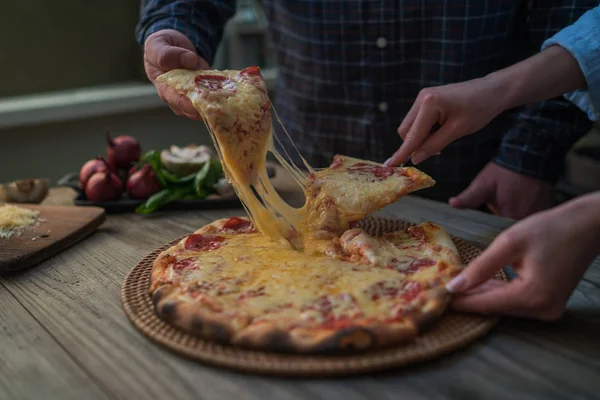 Hot pizza slice with melting cheese on a rustic wooden table. Food ingredients and spices for cooking. Mushrooms, tomatoes, cheese, onion, oil, pepper, salt, basil, olive and delicious italian pizza.