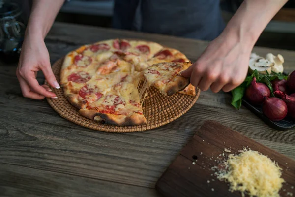 Hot pizza slice with melting cheese on a rustic wooden table. Food ingredients and spices for cooking. Mushrooms, tomatoes, cheese, onion, oil, pepper, salt, basil, olive and delicious italian pizza.