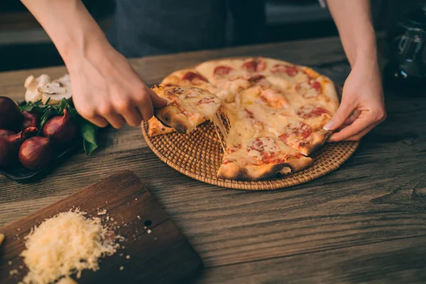 Hot pizza slice with melting cheese on a rustic wooden table. Food ingredients and spices for cooking. Mushrooms, tomatoes, cheese, onion, oil, pepper, salt, basil, olive and delicious italian pizza.