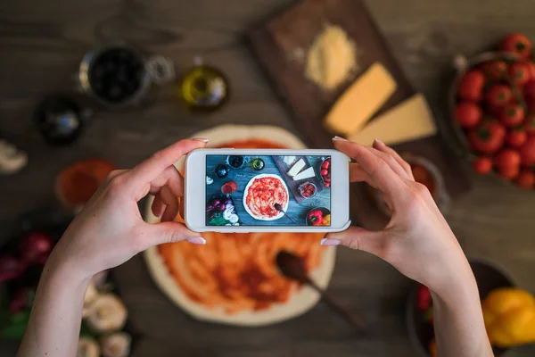 Akıllı telefon elle. Genç kadın, blogger yemek ev mutfak pişirme ve fotoğraf smartphone vasıl yapıyor. Instagram gıda blogger atölye kavramı. Tonlu görüntü.