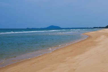Bir güzel boş tropikal plaj dalgalar, kum ve su ile bir açık mavi gökyüzü ile. Yatay kopya alanı. Altın sarı kum parlak güneşli bir günde mavi deniz kenarında ıssız bir sahilde.