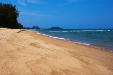Bir güzel boş tropikal plaj dalgalar, kum ve su ile bir açık mavi gökyüzü ile. Yatay kopya alanı. Altın sarı kum parlak güneşli bir günde mavi deniz kenarında ıssız bir sahilde.