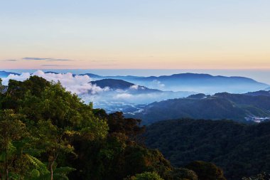 Dağ tepe ön plan üzerinde orman ve köy arasında sisli Vadisi zemin üzerine kıvırcık bulutlar kaplı. Dağlar gündoğumu sırasında. Yaz aylarında güzel doğal peyzaj