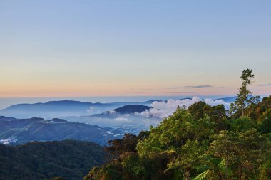 Dağ tepe ön plan üzerinde orman ve köy arasında sisli Vadisi zemin üzerine kıvırcık bulutlar kaplı. Dağlar gündoğumu sırasında. Yaz aylarında güzel doğal peyzaj