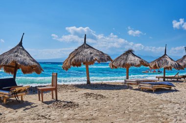 Birkaç plaj şemsiyeleri turkuaz okyanus zemin karşı açık güneşli bir günde thatched. Cennet tropikal Adası'nın kıyısında, saman şemsiye ile boş kum plaj. Seyahat kavramı. 