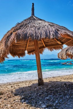 Closeup plaj şemsiyeleri turkuaz okyanus zemin karşı açık güneşli bir günde thatched. Cennet tropikal Adası'nın kıyısında, saman şemsiye ile boş kum plaj. Seyahat kavramı. 