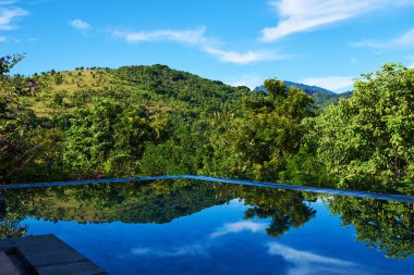 Sonsuzluk havuzu. Lüks dağlar görünümü, derin mavi gökyüzü, yeşil ufuk ve ağaçlar tropikal rahatlatıcı. Luxury resort yaz için rahatla. Kenar Yüzme Havuzu su, güzel manzarayı. Seyahat kavramı.
