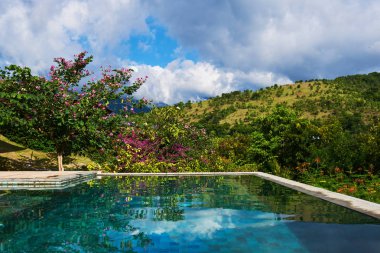 Yaz tatil ve seyahat kavramı. Lüks villa, sonsuzluk havuzu bakan görünümü dağlar ve arka planda mavi gökyüzü. Tropikal ağaçlar, beyaz bulut ve yüzme havuzu üzerinde mavi gökyüzünün yansıması. 