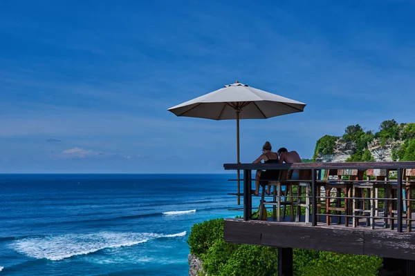 青い海を背景に若いカップルの背面します 幸せなカップルは 夏の休暇中に美しい景色をリラックスします オーシャン ビューの前に穏やかで平和なリラックスした午後を楽しんでください — ストック写真