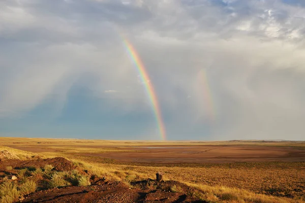 Rainbow in sky among  landscape over the boundless savannah, summer nature background, blue sky with clouds for summer adventure. The rainbow crosses the sky over desert. The concept of exotic tourism.