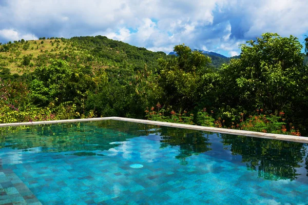Infinity pool. Luxury relaxing mountains view, deep blue sky, green horizon and a tropical trees. Luxury resort for summertime relax. Edge swimming pool water, enjoying beautiful view. Travel concept.