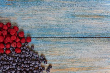 Olgun sulu organik çilek mavi rustik masada grubudur. Lezzetli doğa vejetaryen madde. Yaban mersini ve ahududu. Sağlıklı yaz meyveleri, antioksidanlar. Kopya alanı ile üstten görünüm.