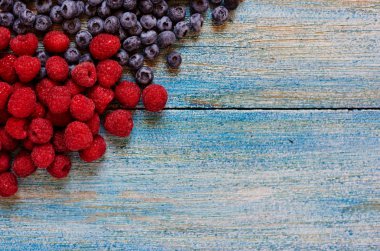 Olgun sulu organik çilek mavi rustik masada grubudur. Lezzetli doğa vejetaryen madde. Yaban mersini ve ahududu. Sağlıklı yaz meyveleri, antioksidanlar. Kopya alanı ile üstten görünüm.