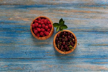 Mavi rustik ahşap masa üzerinde kırmızı taze ahududu ile top. Ahşap kase taze bahçe ahududu. Sağlıklı kahvaltı kavramı. Seçici odak.