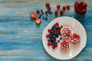 Parti gıda. Berry mousse ile Mini kek, karamel ve taze meyveler. Yaban mersini ve krem peynir rustik ahşap arka plan üzerinde plaka üzerinde taze ev yapımı turtalar. Üstten görünüm. Seçici odak