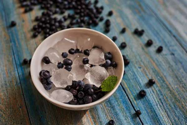 On the blue vintage table light falls through slightly parted blinds on the table is a plate of ice which are berries