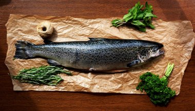 Somon karkas yakınındaki yeşillik, maydanoz, biberiye ve mantar kahverengi parşömen kağıt üzerinde yalan