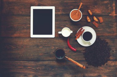 Karanlık dokusal ahşap bir masa üzerinde bir tablet yatıyor, bir fincan sütlü kahve Cezve artıkları güçlü siyah kahve