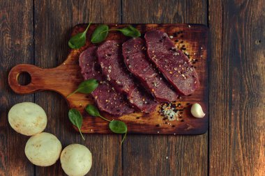 Ham sığır eti biftek ile baharat rustik ahşap arka plan üzerinde kavurma için hazır. Taze mermer et biftek otlar, sarımsak, zeytinyağı, tüm biber ve kaya tuzu ile. Kopya alanı ile üstten görünüm.