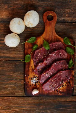 Ham sığır eti biftek ile baharat rustik ahşap arka plan üzerinde kavurma için hazır. Taze mermer et biftek otlar, sarımsak, zeytinyağı, tüm biber ve kaya tuzu ile. Kopya alanı ile üstten görünüm.