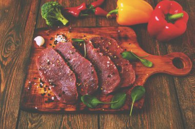 Sığır filetosu biftek ile baharat ve sebzeler ahşap tahta üzerinde. Bell ve biber biber, ot, tuz. dengeli beslenme, protein ve lif oncept. Üstten görünüm kopya alanı ile. Vintage tarzı.